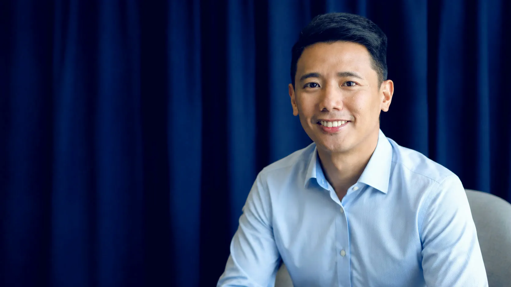 Si Coach Paolo Castro, nakangiti sa isang studio portrait na may navy na kurtina sa likod