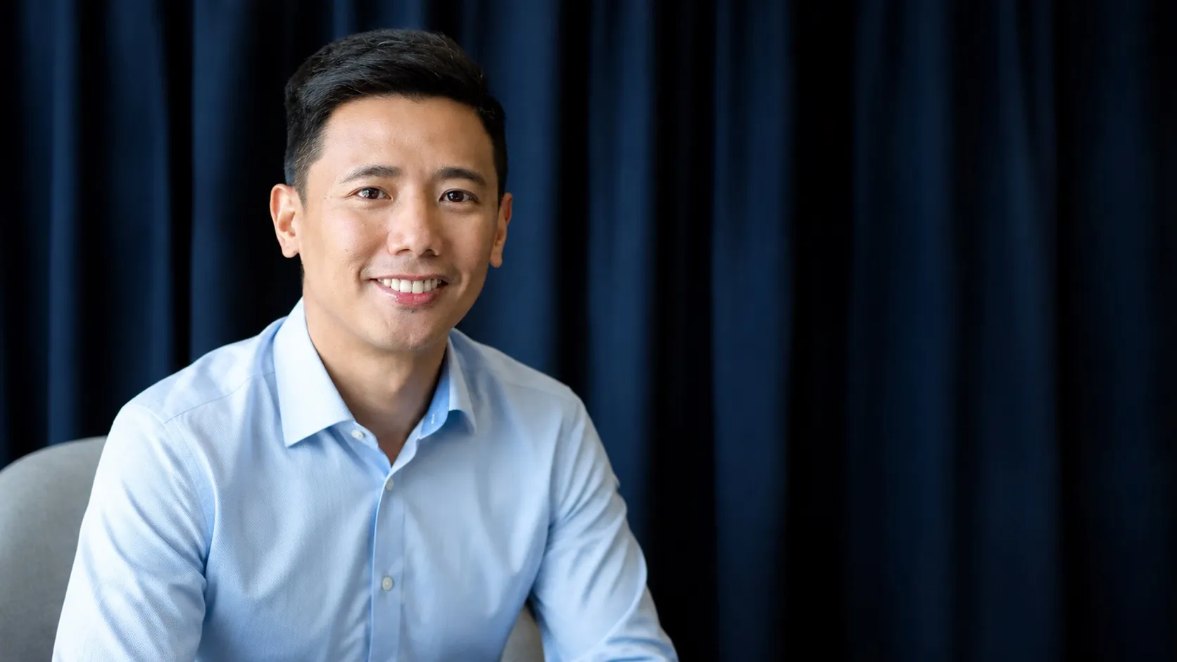 Si Coach Paolo Castro, nakangiti sa studio portrait na may navy na kurtina sa likod